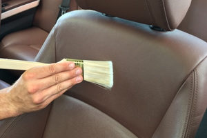 Close up of hand using a brush to clean and remove dust or dirt on the car seat